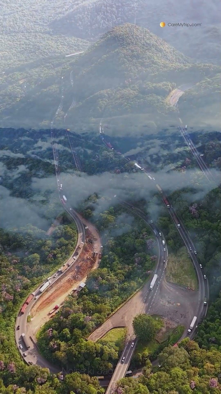 Aerial view of a mountain road winding through forest under low clouds
