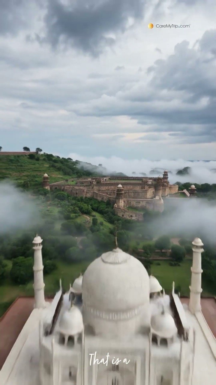 The Taj Mahal dome with a fort on a green hill in the mist behind it